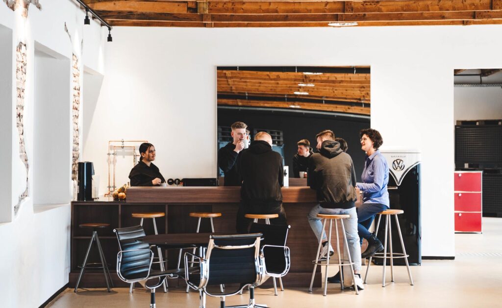 Mitarbeitende und Auszubildende von STROHBECKE sitzen gemeinsam an der Kaffeebar und unterhalten sich – Symbol für Teamgeist und offene Unternehmenskultur in der Ausbildung.