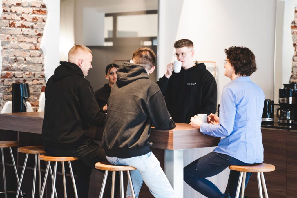 Mitarbeitende von STROHBECKE unterhalten sich bei einer Kaffeepause an der Bar – Symbol für Gemeinschaft, Austausch und gelebte Teamkultur.