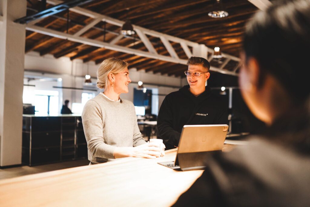 Zwei Mitarbeitende von STROHBECKE stehen an einem Tisch im modernen Büro, unterhalten sich und lächeln – Symbol für offene Kommunikation und Teamarbeit.