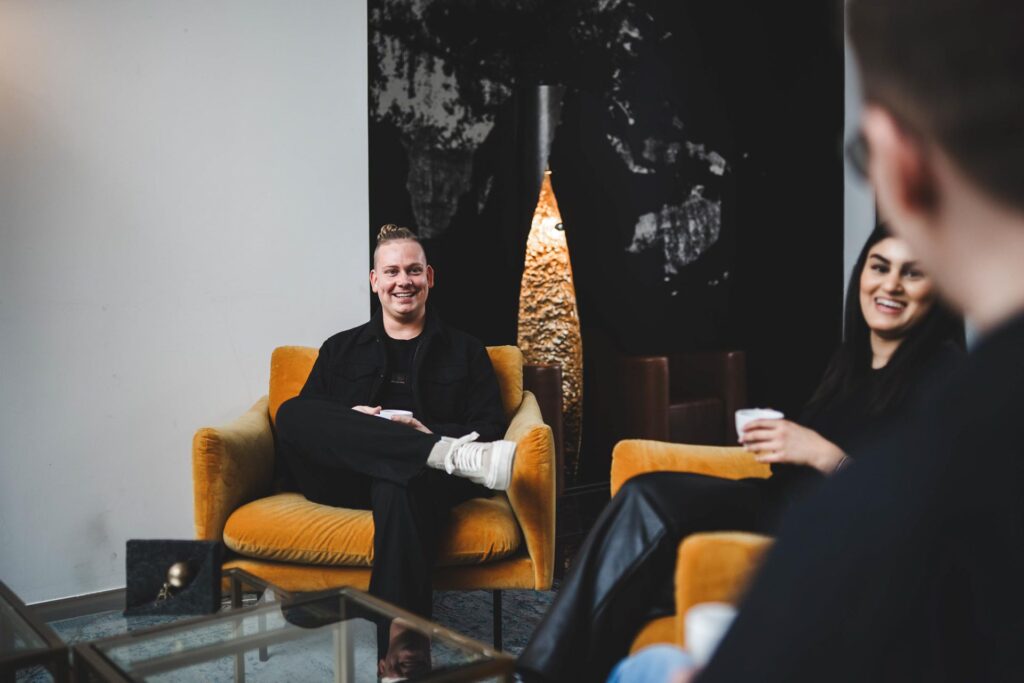 Mitarbeiterinnen und Mitarbeiter von STROHBECKE sitzen in gelben Sesseln im Loungebereich in Herford und führen ein internes Teammeeting.