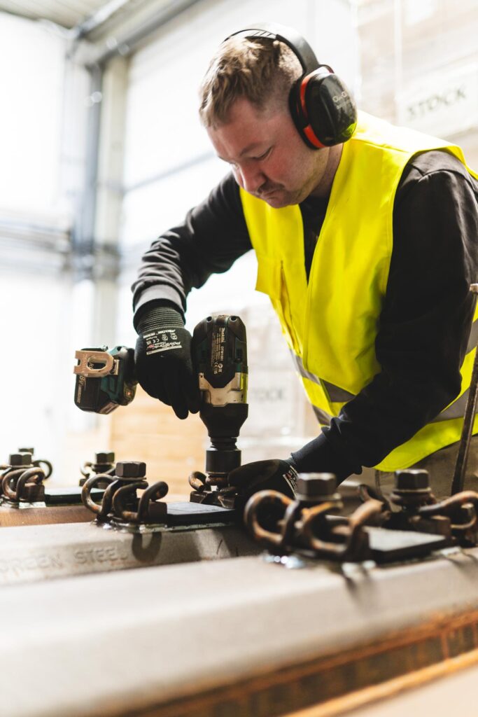 Ein Mitarbeiter mit Gehörschutz montiert konzentriert Metallteile an einem Arbeitsplatz in der Lagerhalle von STROHBECKE.