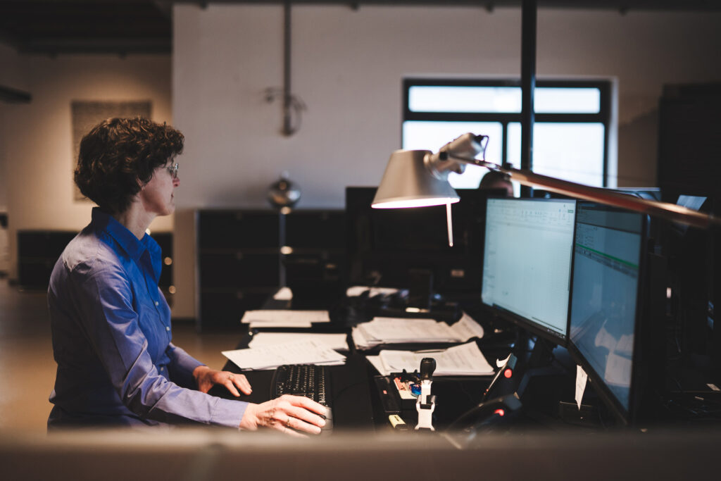 Mitarbeiterin arbeitet konzentriert am Computer an mehreren Monitoren im Büro.